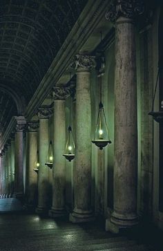 a long hallway with columns and lights on the ceiling in an old building at night