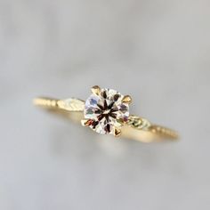 a yellow gold engagement ring with a round diamond in the center on a white background