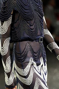 a woman walking down a runway wearing a black and white dress with beading on it