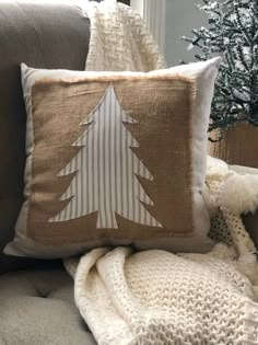 a white christmas tree pillow sitting on top of a gray couch next to a blanket