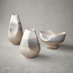 three white vases sitting next to each other on top of a cement flooring