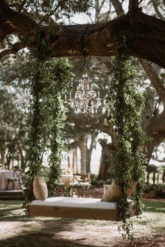 a chandelier hanging from a tree over a bed in the middle of a park