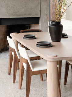 a wooden table topped with white chairs and a vase filled with flowers next to a fire place