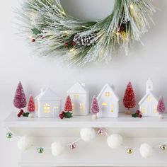 christmas decorations are displayed on a mantle in front of a wreath and small white houses