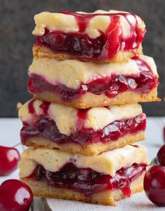 cherry cheesecake bars stacked on top of each other with fresh cherries around them