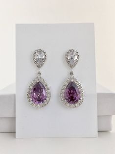 a pair of purple and white earrings with diamonds on top of a white box next to it