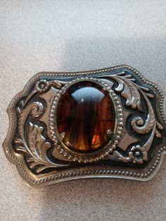 vintage silver tone belt buckle with natural stone cabochaon. VINTAGE SILVER TONE CABOCHON IN MIDDLE RESEMBLES TIGER'S EYE MINERAL WITH STRIATIONS  OF SOMETHING ELSE MIXED IN. I REALLY DON'T KNOW WHTAT THE ENTIRE STONE IS, BUCKLE MEASURES 3 1/2" X 2 1/2" SOME CORROSION EVIDENT ON METAL BRACKET HOLDING STONE IN ( SHOWS IN PHOTOS) VERY NICE PIECE FAST SHIPPING  THANKS FOR LOOKING Engraved Silver Belt Buckles As Gift, Formal Brown Concho Jewelry, Vintage Brown Jewelry With Antique Buckle, Adjustable Brown Jewelry With Antique Buckle, Silver Concho Belt Buckles As Gift, Handmade Western Belt Buckles For Gift, Handmade Western Belt Buckles As Gift, Antique Silver Belt Buckles Collectible, Antique Silver Collectible Belt Buckles