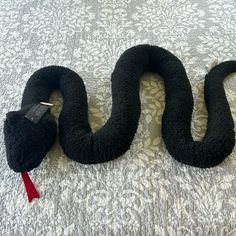 a stuffed snake laying on top of a bed next to a red tag in its mouth