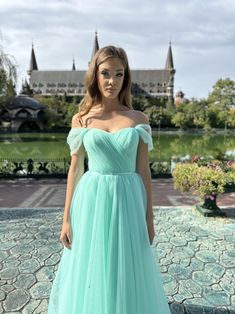 a woman in a blue dress standing on a stone walkway with a castle in the background