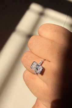 a person's hand holding a ring with a diamond in it and the light shining on them