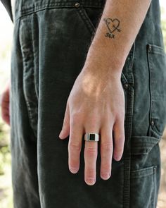 a man with a heart tattoo on his left hand, wearing a ring and jeans