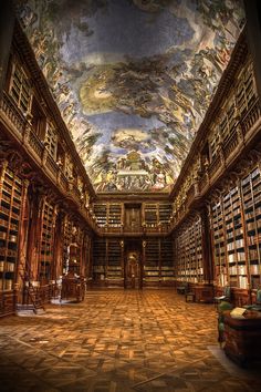 the library is full of books and many paintings on the walls, including an elaborately painted ceiling