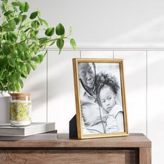 a wooden table topped with a vase filled with flowers and a framed photo next to a plant