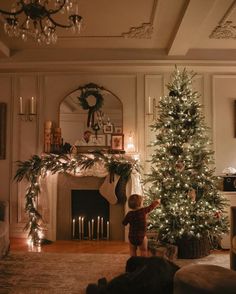 a little boy standing next to a christmas tree in front of a fire place with candles