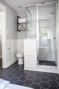 a white bathroom with black tile flooring and shower stall, along with shelves on the wall