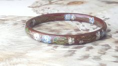 "Vintage nature inspired floral design cloisonne enameled brass bangle bracelet. The background color is a bordeaux/ chocolate brown, the flowers are blue and lilac with white centers, the stems and leaves are green. The bracelet is in very good condition. See photos for details. 4mm, 2-5/8\"ID" Burgundy Background, Brass Picture Frames, Golden Rutilated Quartz, Vintage Floral Design, Sunflower Pendant, Brass Bangle, Vintage Texture, Mocha Brown, Cloisonne Enamel