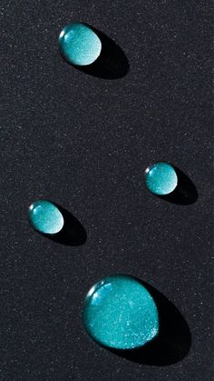 three blue bubbles floating in the air on top of a black surface with white speckles