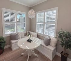 a white table and bench in a room with two windows that have shutters on them