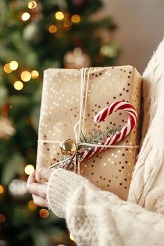 a woman holding a wrapped present in front of a christmas tree with a candy cane