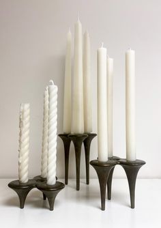 several white candles are lined up next to each other on black stands, against a gray background