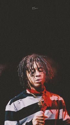 a man with dreadlocks standing in front of a black background wearing a striped shirt