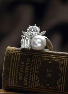 a pearl and diamond ring sitting on top of an old book