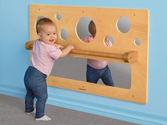 two children playing with a wooden wall mounted mirror in a playroom at the same time