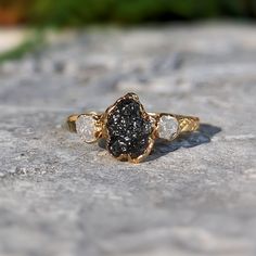 a gold ring with black and white stones on it sitting on top of a rock