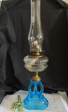 a blue glass table lamp sitting on top of a white cloth next to a green plant