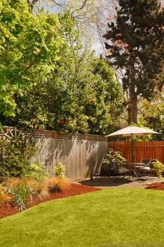 a backyard with a wooden fence, grass and an umbrella in the middle of it