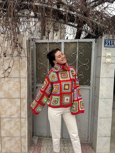 a woman standing in front of a door with her eyes closed and wearing a colorful crocheted sweater