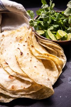 some tortillas are next to a bowl of cilantro