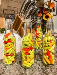 four glass bottles filled with vegetables on top of a counter next to utensils