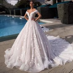 a woman standing in front of a pool wearing a wedding dress with flowers on it