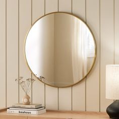 a round mirror sitting on top of a wooden dresser next to a lamp and book