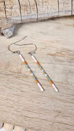 two white and orange beaded earrings sitting on top of a piece of drift wood