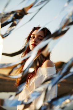 a woman standing in front of a metal fence with her hair blowing in the wind