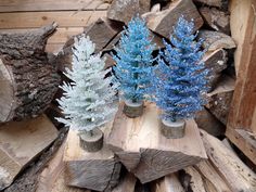 three small blue trees sitting on top of wooden logs