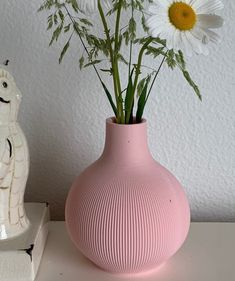 a pink vase with daisies in it next to a small white horse figurine