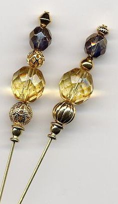 two yellow and brown beads on a white surface next to a silver pins with gold tips