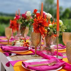 the table is set with orange and pink flowers in vases, napkins, and candles