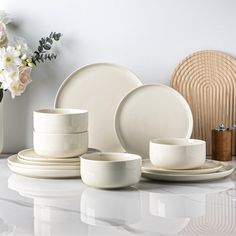 white dishes and cups sitting on top of a counter next to a vase with flowers