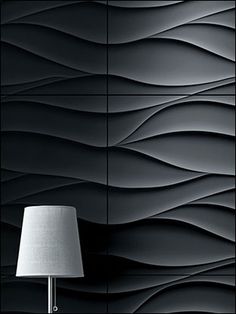 a lamp is next to a black wall with wavy lines on it and a white shade