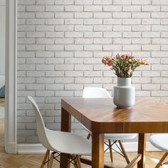 a wooden table and white chairs in front of a brick wall with flowers on it