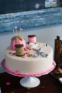 a white cake with pink icing and spools of thread on it, sitting on a table