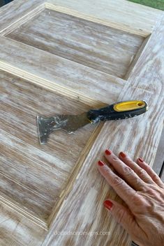 a woman's hand is holding a knife on top of a wooden door frame