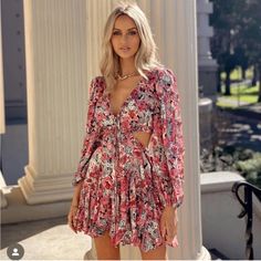 a woman standing in front of columns wearing a pink floral dress with cut out sides