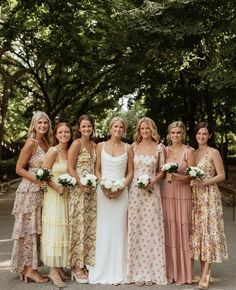 a group of women standing next to each other wearing dresses and holding bouquets in their hands