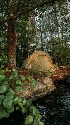 a tent pitched up next to a river in the woods