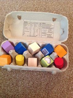 an egg carton filled with different colored wooden blocks on the floor next to a brown carpet